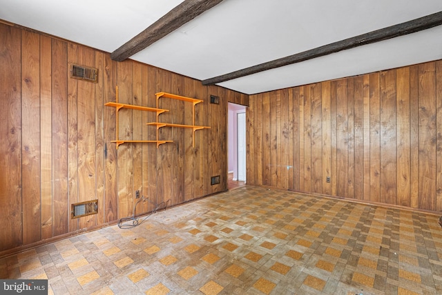 unfurnished room featuring wood walls, visible vents, and beam ceiling