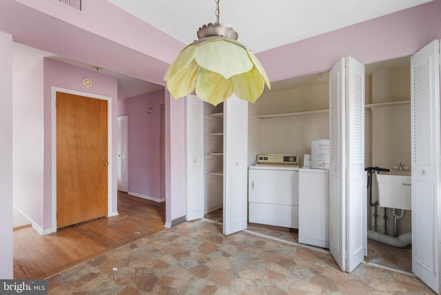 laundry area with washing machine and clothes dryer, stone finish flooring, a sink, laundry area, and baseboards