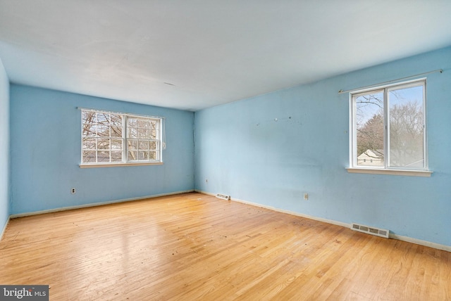 empty room featuring plenty of natural light, visible vents, and wood finished floors