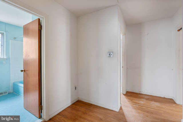 hall with light wood-type flooring, visible vents, and baseboards