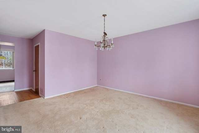 carpeted spare room with baseboards and an inviting chandelier