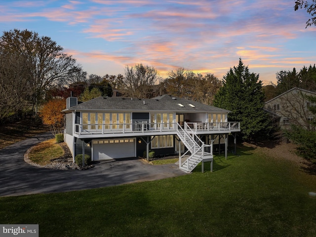 back of house at dusk with a lawn, driveway, stairs, a wooden deck, and a chimney