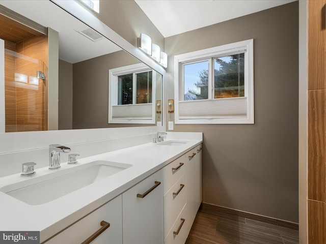 bathroom featuring double vanity, baseboards, a tile shower, and a sink