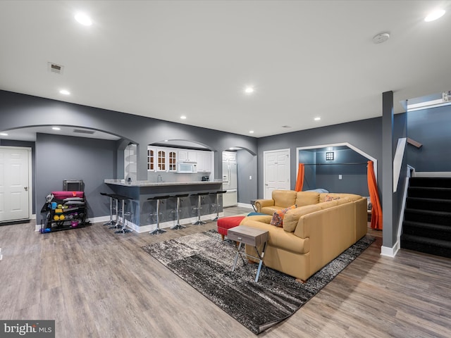 living room featuring wood finished floors, visible vents, recessed lighting, arched walkways, and stairs