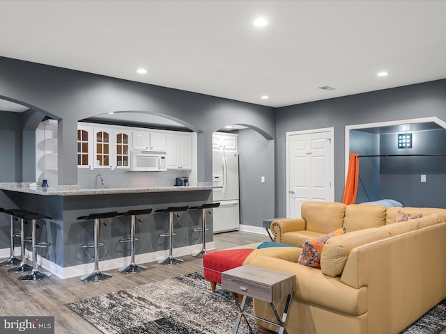 living area featuring recessed lighting, baseboards, arched walkways, and light wood-style flooring