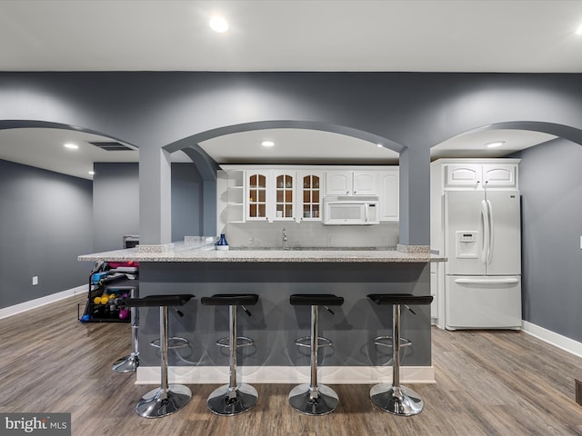 kitchen with white cabinets, white appliances, a breakfast bar area, and light stone countertops