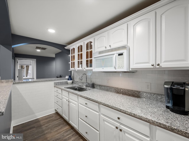 kitchen featuring white microwave, a sink, glass insert cabinets, light stone countertops, and dark wood-style flooring