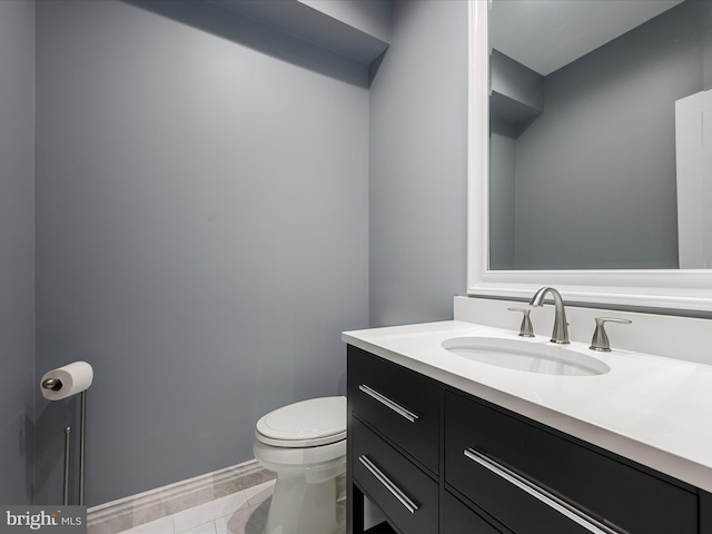 half bathroom with vanity, tile patterned floors, toilet, and baseboards