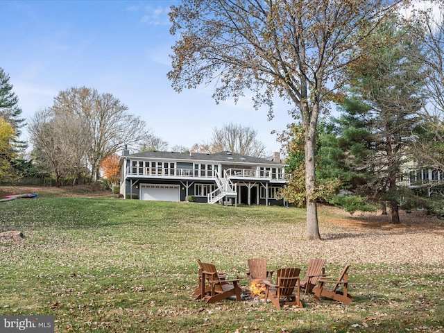 rear view of house featuring a lawn, stairway, a fire pit, a wooden deck, and a garage