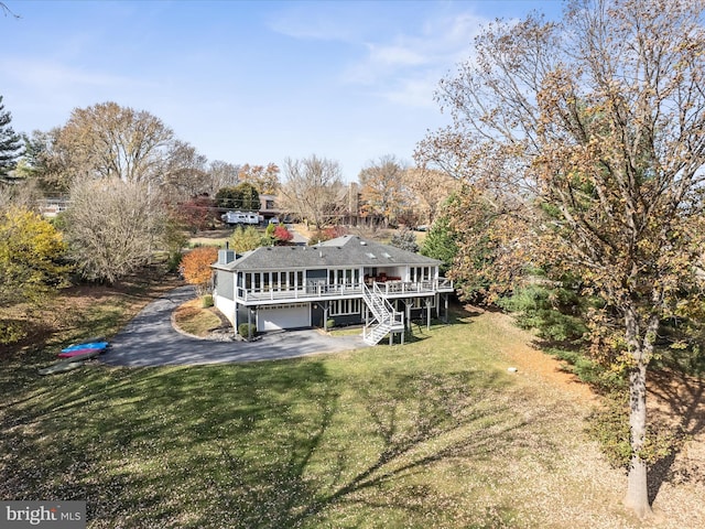 rear view of house with an attached garage, stairway, a yard, a deck, and driveway