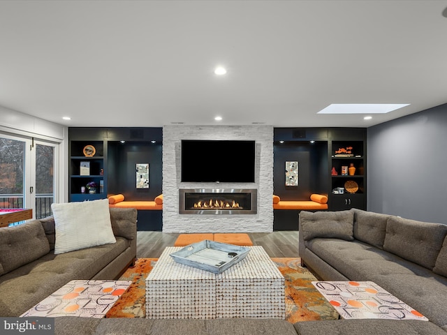 living area with a skylight, built in shelves, wood finished floors, and a fireplace