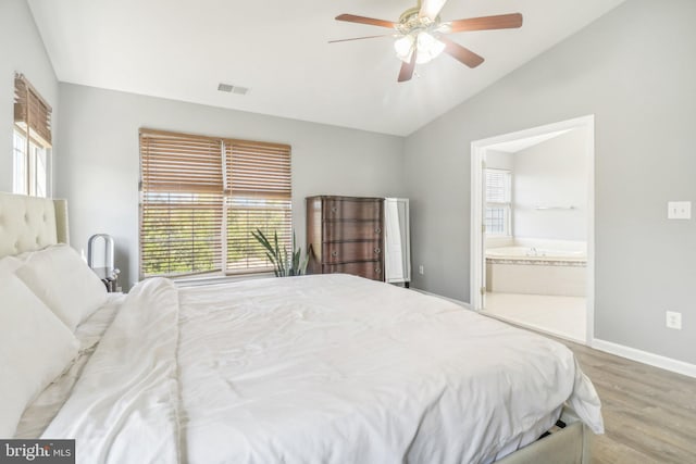 bedroom featuring baseboards, visible vents, wood finished floors, ensuite bathroom, and vaulted ceiling