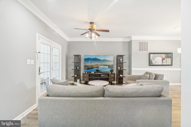 living area with baseboards, light wood-style floors, visible vents, and crown molding