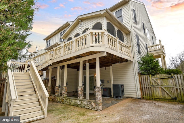 back of property at dusk featuring a patio, central air condition unit, a gate, a wooden deck, and stairs