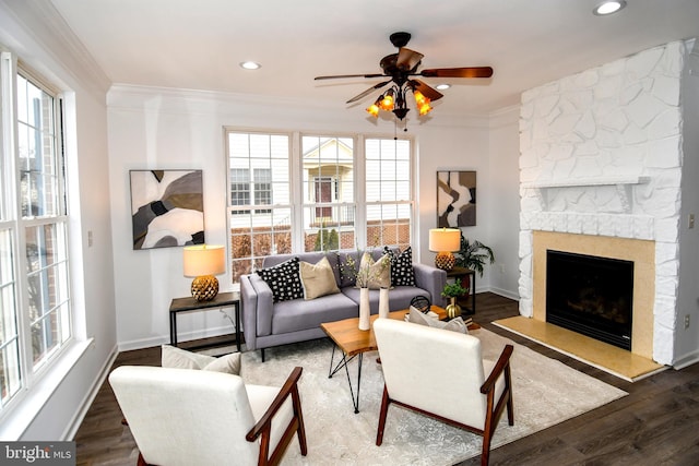 living room featuring baseboards, wood finished floors, crown molding, a stone fireplace, and recessed lighting