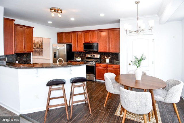 kitchen with stainless steel appliances, a breakfast bar, a peninsula, decorative backsplash, and dark stone counters