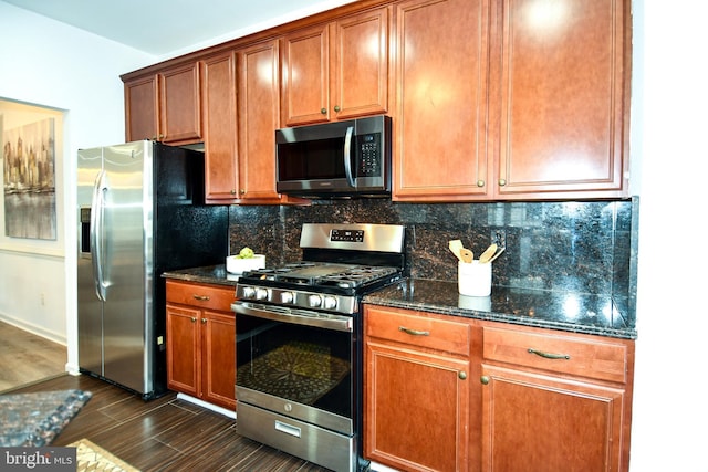 kitchen with brown cabinets, dark wood finished floors, tasteful backsplash, appliances with stainless steel finishes, and dark stone counters