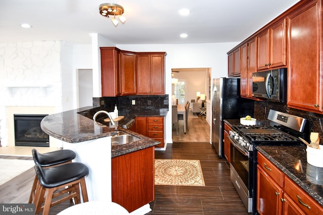 kitchen with stainless steel appliances, dark wood-type flooring, a peninsula, a sink, and decorative backsplash