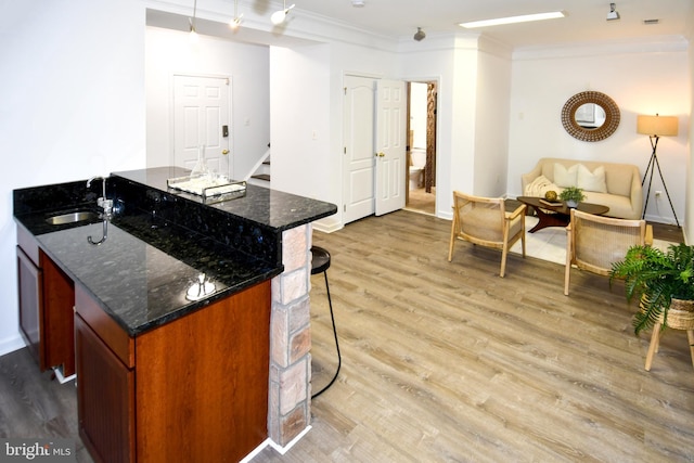 kitchen featuring light wood-style flooring, a breakfast bar area, ornamental molding, and a sink