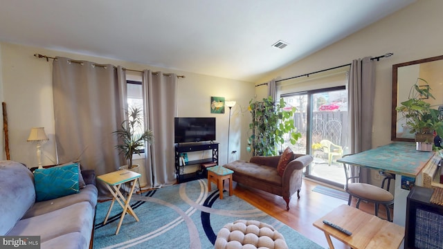 living area with visible vents, vaulted ceiling, and wood finished floors