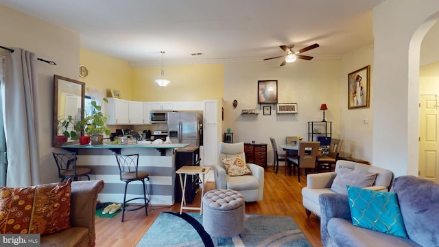 living area with light wood-type flooring, visible vents, arched walkways, and a ceiling fan