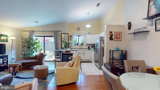 living area featuring light wood-type flooring, high vaulted ceiling, visible vents, and ornamental molding