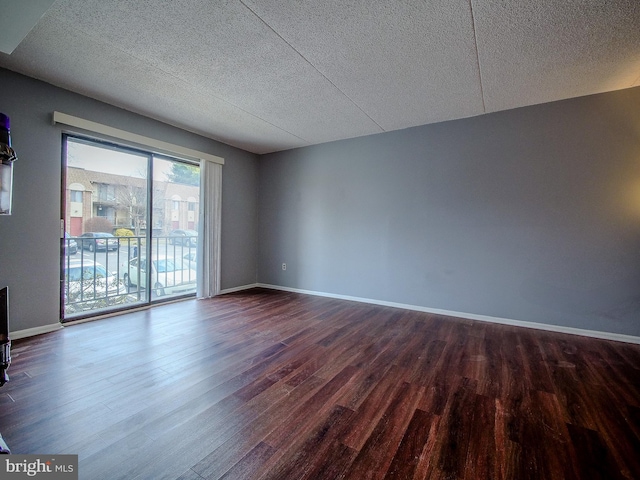 unfurnished room with a textured ceiling, dark wood finished floors, and baseboards