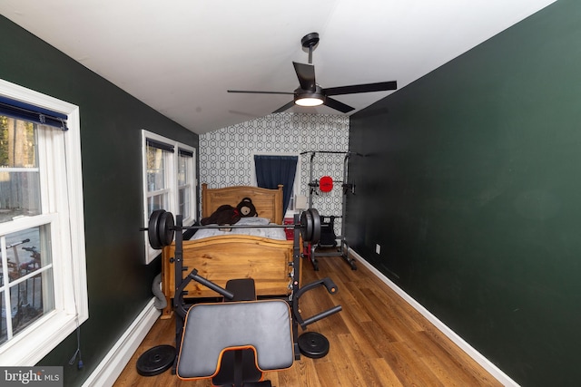 exercise area featuring wood finished floors, a ceiling fan, baseboards, lofted ceiling, and an accent wall