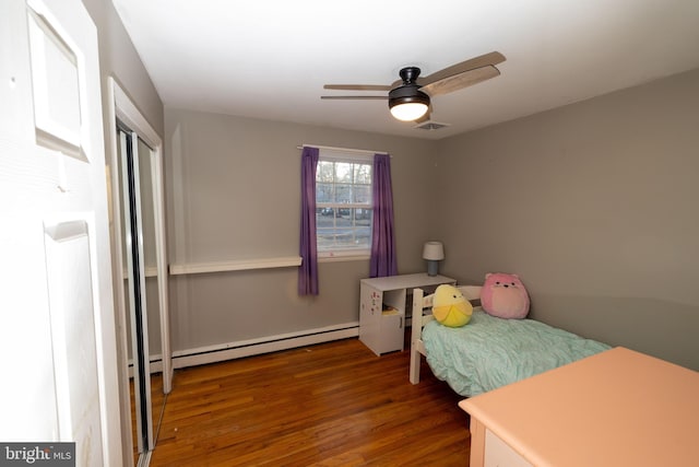 bedroom featuring a baseboard heating unit, wood finished floors, visible vents, and a ceiling fan