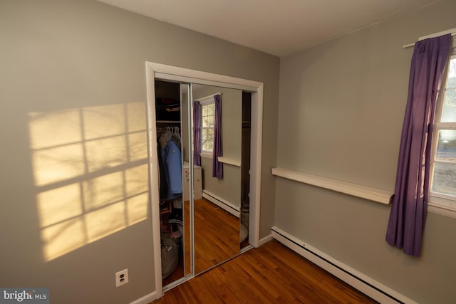 unfurnished bedroom featuring a baseboard heating unit, baseboards, baseboard heating, wood finished floors, and a closet