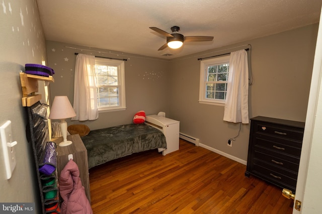 bedroom with a baseboard radiator, multiple windows, visible vents, and wood finished floors