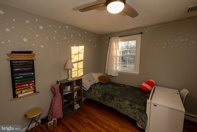 bedroom featuring visible vents, baseboard heating, ceiling fan, and wood finished floors