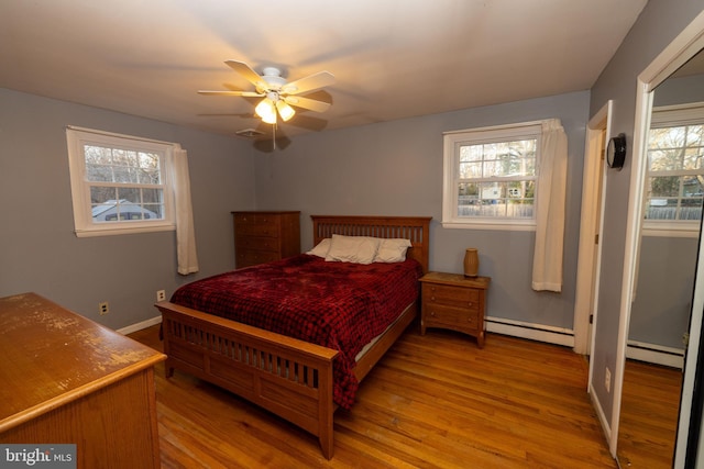 bedroom with visible vents, a baseboard heating unit, wood finished floors, baseboards, and ceiling fan