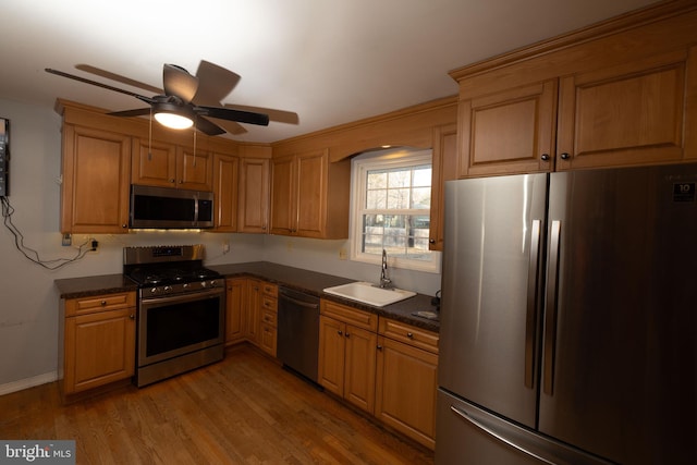 kitchen featuring light wood-style flooring, a sink, ceiling fan, stainless steel appliances, and dark countertops