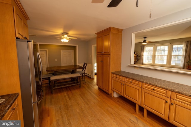 kitchen with brown cabinetry, light wood-style floors, a ceiling fan, and freestanding refrigerator