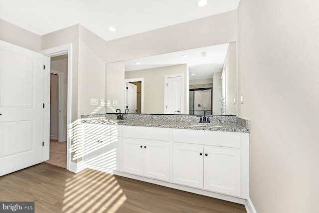 full bath with double vanity, a sink, a shower stall, and wood finished floors