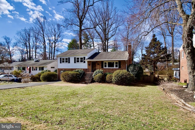 tri-level home with aphalt driveway, a chimney, a front lawn, and brick siding