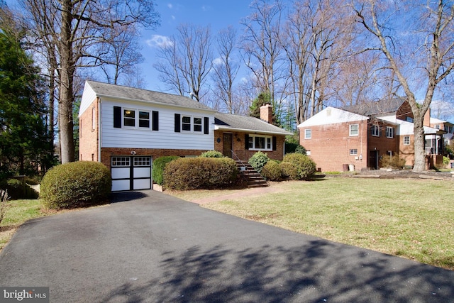 tri-level home with aphalt driveway, an attached garage, brick siding, a chimney, and a front yard