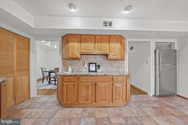 kitchen featuring stone finish floor, visible vents, backsplash, and freestanding refrigerator