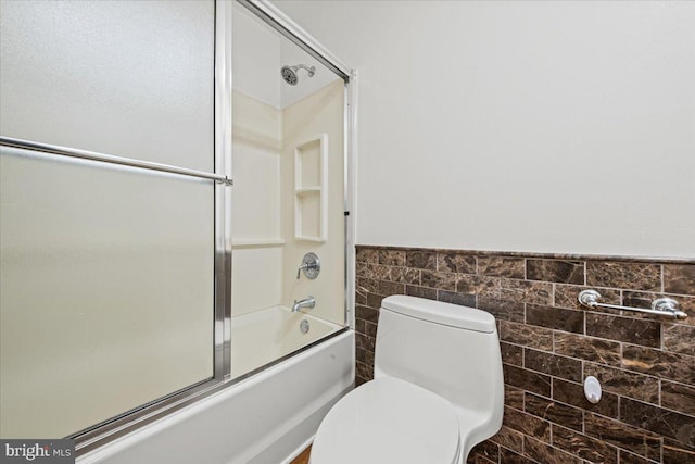 full bathroom featuring toilet, enclosed tub / shower combo, tile walls, and wainscoting