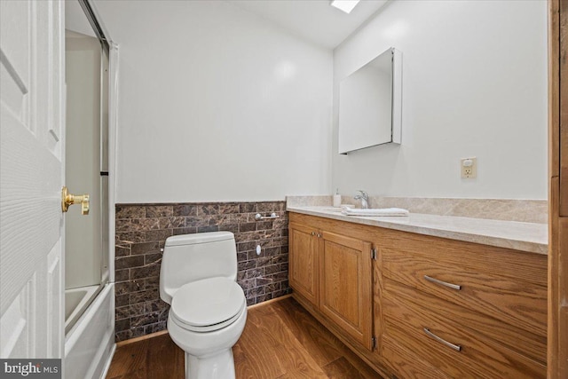 bathroom with a wainscoted wall, tile walls, toilet, vanity, and wood finished floors