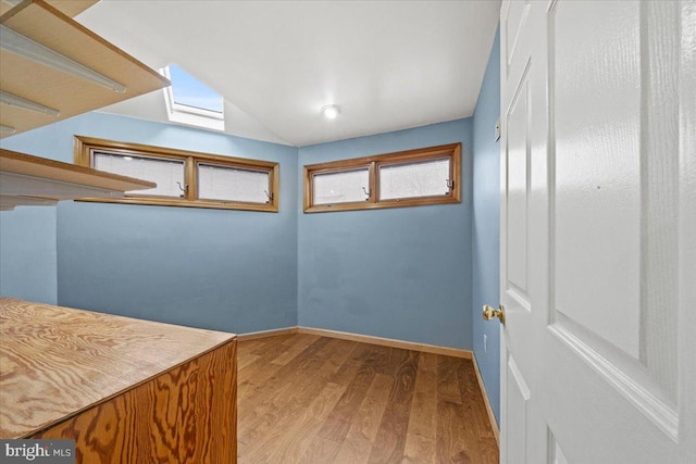 interior space with lofted ceiling with skylight, baseboards, and wood finished floors