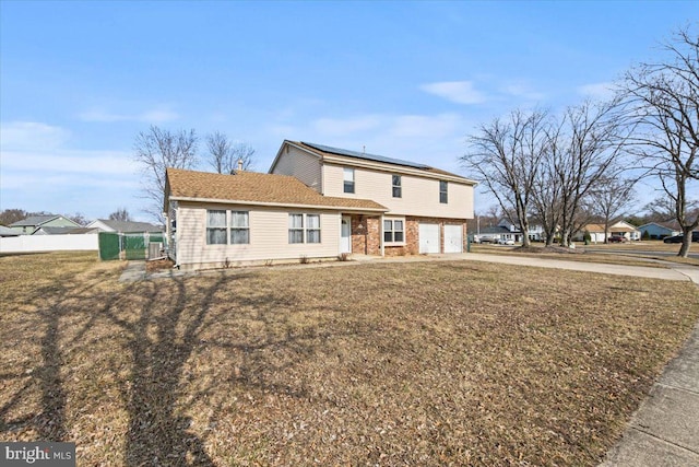 view of front of house with an attached garage, brick siding, fence, driveway, and roof mounted solar panels