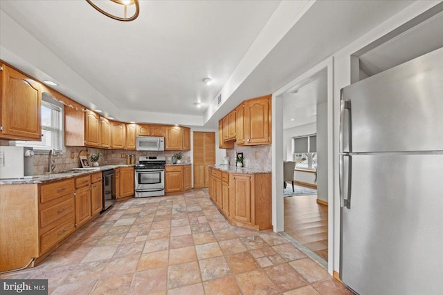 kitchen featuring stone finish floor, light stone counters, appliances with stainless steel finishes, a sink, and backsplash