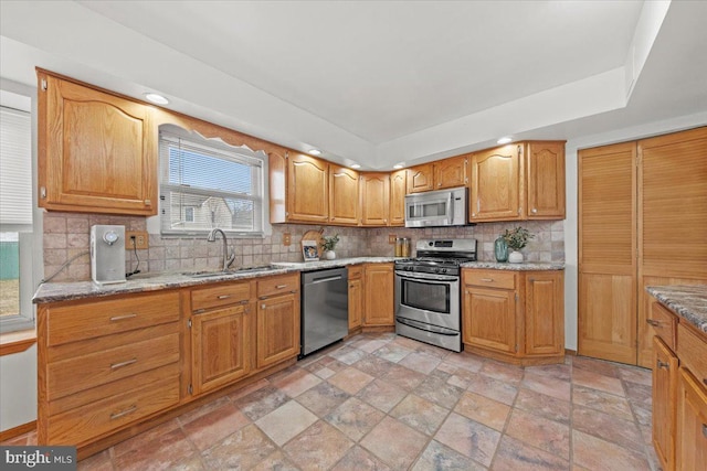 kitchen with appliances with stainless steel finishes, a sink, light stone counters, and decorative backsplash