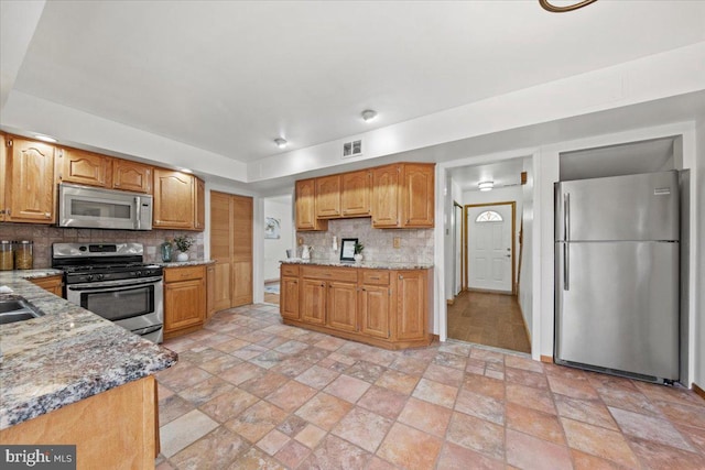 kitchen with tasteful backsplash, light stone counters, stainless steel appliances, and stone finish flooring