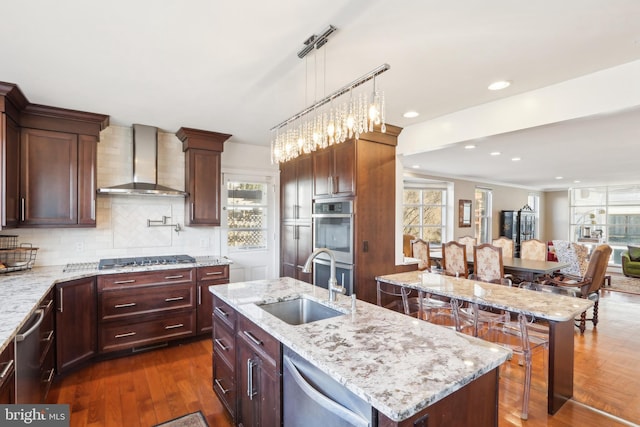 kitchen featuring dark wood-type flooring, a sink, tasteful backsplash, stainless steel appliances, and wall chimney exhaust hood