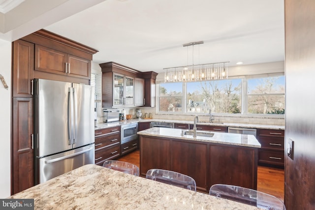 kitchen with a center island with sink, light stone counters, decorative light fixtures, a sink, and appliances with stainless steel finishes