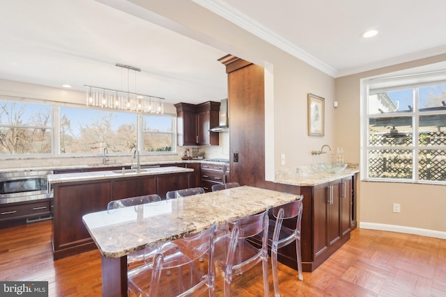 kitchen featuring crown molding, an island with sink, stainless steel appliances, wall chimney exhaust hood, and a sink