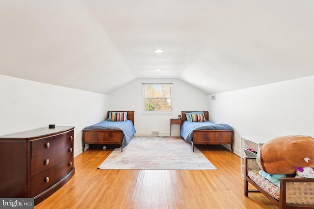 bedroom featuring visible vents, baseboards, light wood-style floors, and vaulted ceiling